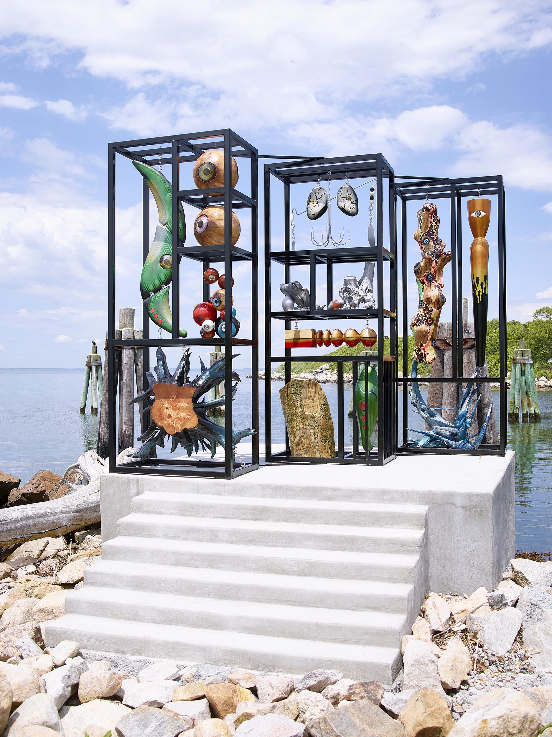 Sculptural work made with painted steel and resembling a vertical multi-tiered tackle box placed by the sea. The structure contains 14 wooden sculptures that derive inspiration from the concept and design of