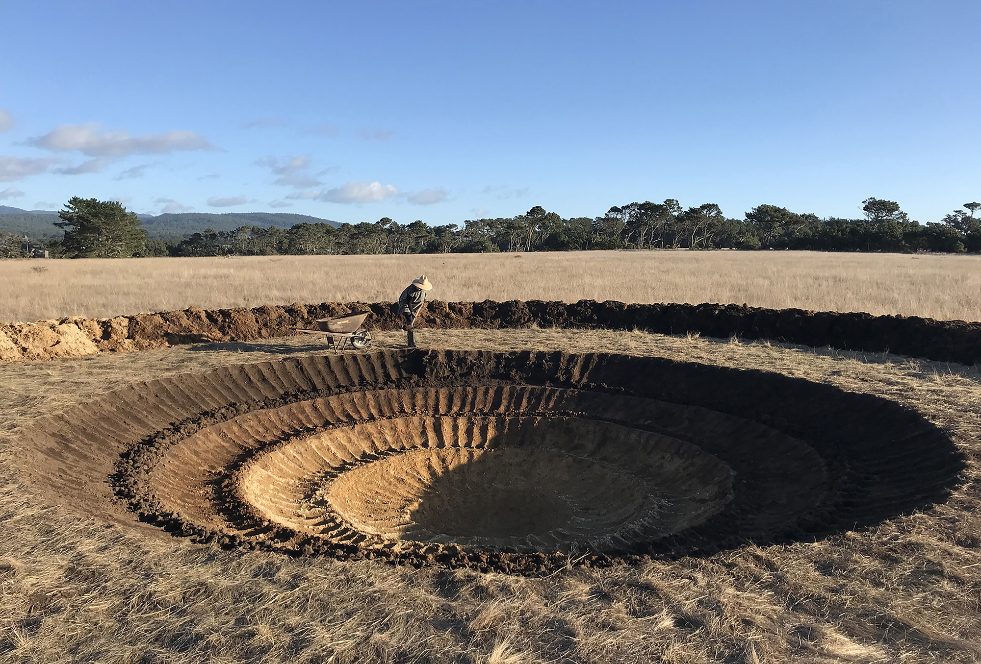 A crater stretches the width of the image and at the far side, the artist is seen digging with a shovel.